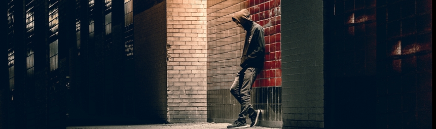 A hooded teenager leaning against a wall on a dark street