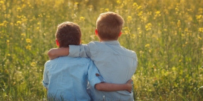 Two boys in a firld facing away from camera hugging